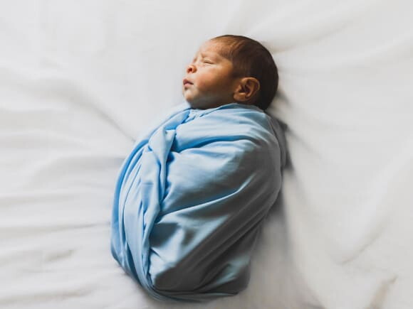 bebê sorrindo, com as mãos levantadas e parcialmente coberto por uma manta azul