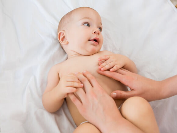 bebê usando fralda e um adulto com as mãos sob a barriga do bebê