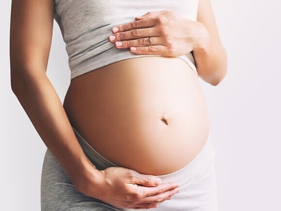 Imagem de mulher com as mãos na barriga para representar eritroblastose fetal.