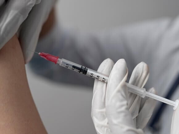 Imagem de um profissional de saúde aplicando uma injeção no braço de um pessoa