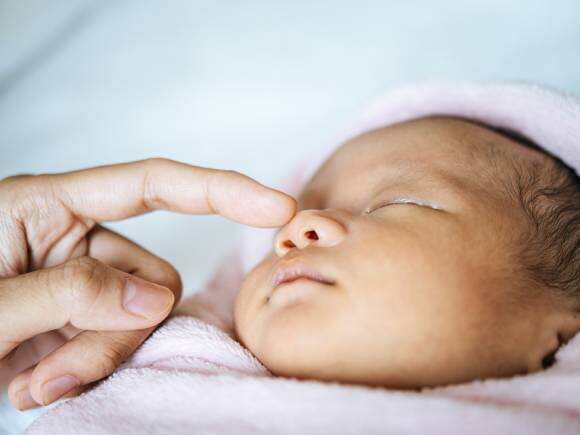 mão de um adulto tocando o rosto de um recém-nascido