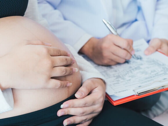 Médico com uma prancheta nas mãos fazendo anotações enquanto uma mulher grávida está sentada na cama