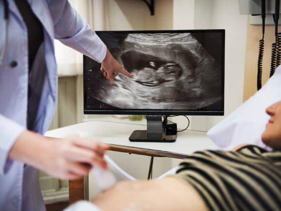 mulher grávida fazendo ultrassom, ao fundo uma tela exibindo a imagem do exame