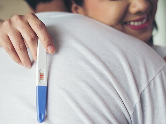 Uma mulher abraçando o marido enquanto segura um teste de gravidez