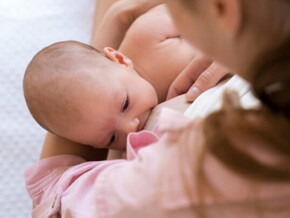 Mulher vestindo blusa rosa segurando bebê enquanto amamenta 