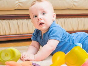 Bebê deitado de bruços no chão com alguns brinquedos em sua volta