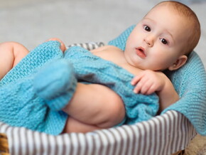 Imagem de um bebê aconchegado em um cobertor azul dentro de uma cesta