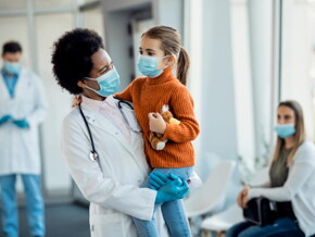 médica sorrindo enquanto segura uma criança em um ambiente hospitalar