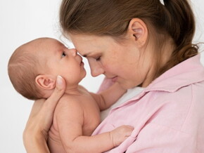 Mãe segurando a filha recém nascida no colo e com os rostos juntos.