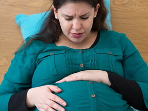 Mulher grávida sentada na cama com semblante de preocupação embalando sua barriga