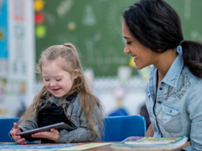 Criança com Síndrome de Down segurando um tablet ao lado da professora na escola