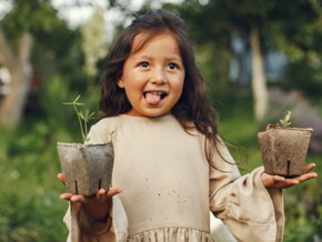 menina sorri e mostra a língua enquanto segura dois vasos de plantas
