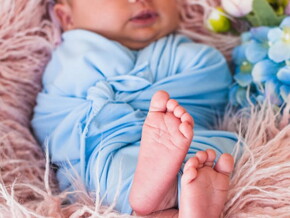 Ensaio fotográfico de bebê recém nascido deitado usando roupa azul claro.