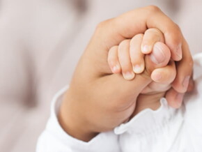 Imagem de uma pessoa segurando suavemente a mãozinha do bebê