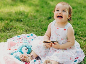 Menina de aproximadamente um ano usando vestido florido e sentada na grama de um parque.