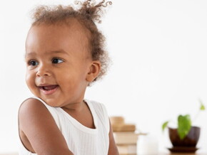 Bebê de perfil sorrindo e vestindo blusa branca