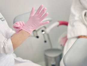 Paciente sentada em cadeira ginecologia enquanto médica se prepara para examiná-la