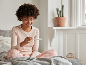 Mulher sentada na cama olhando feliz para um teste de gravidez