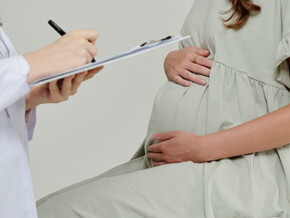 Um médico faz anotações em uma prancheta enquanto uma mulher grávida está sentada em uma cadeira
