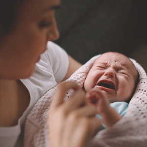 Woman holding a crying baby, trying to soothe him.