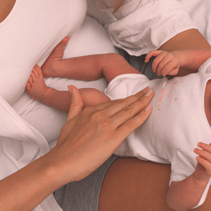 Baby lying on her back, having her belly caressed by a mother's hand.