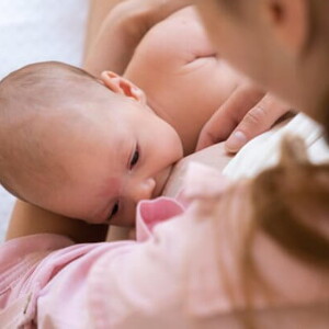 Mulher vestindo blusa rosa segurando bebê enquanto amamenta 