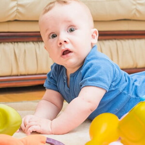 Bebê deitado de bruços no chão com alguns brinquedos em sua volta