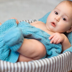 Imagem de um bebê aconchegado em um cobertor azul dentro de uma cesta
