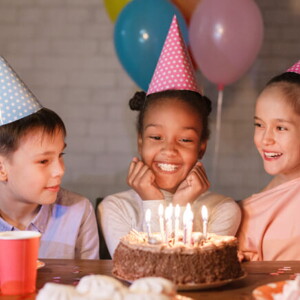 diversas crianças sorriem ao redor de bolo sobre mesa