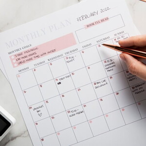 Na imagem, uma mão segura uma caneta diante de um calendário do mês