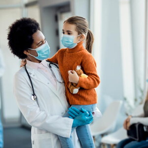 médica sorrindo enquanto segura uma criança em um ambiente hospitalar