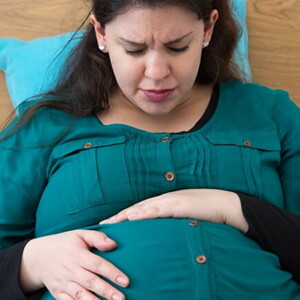 Mulher grávida sentada na cama com semblante de preocupação embalando sua barriga