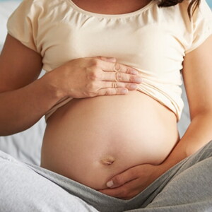 Gestante sentada na cama com as pernas cruzadas enquanto acaricia a barriga com as duas mãos.