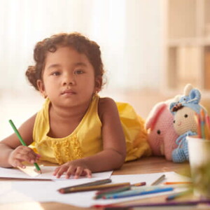 menina com blusa amarela segurando um lápis e desenhando em um caderno