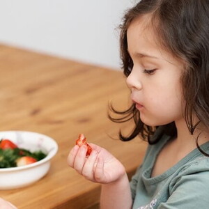 Criança pegando um alimento que está no prato na sua frente 