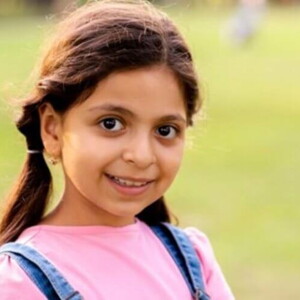 Menina usando macacão jeans e camiseta rosa sorrindo em um gramado verde