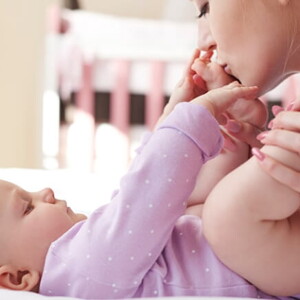 Mãe embalando carinhosamente as perninhas do seu bebê que está deitado na cama