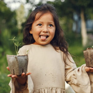 menina sorri e mostra a língua enquanto segura dois vasos de plantas