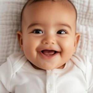 Bebê usando roupa branca em cima de um edredom sorrindo