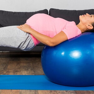 Gestante com as costas apoiadas em uma bola inflável praticando fisioterapia pélvica.