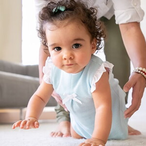 Menina vestindo vestido azul aprendendo a engatinhar