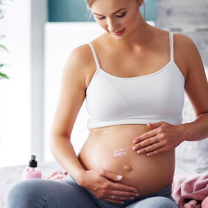 gestante sentada passando creme na barriga