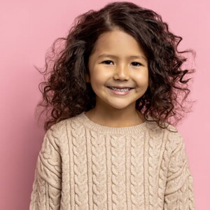 Menina de cabelo ondulado sorrindo em frente a uma parede cor de rosa.