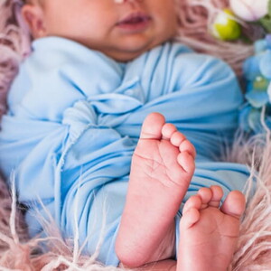 Ensaio fotográfico de bebê recém nascido deitado usando roupa azul claro.