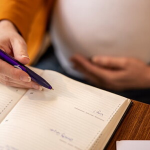 Imagem de um mulher grávida fazendo anotações em uma agenda