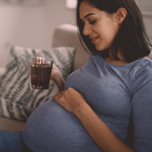 Pregnant woman on a couch, drinking tea and smiling.