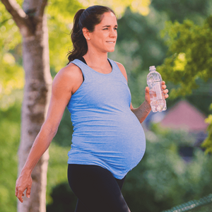 Pregnant woman exercising outdoors, holding a water bottle