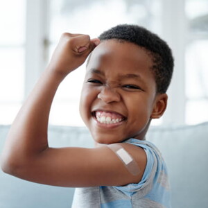 menino feliz sorri com braço levantado e um band-aid