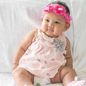 Bebê recém nascida usando vestido florido e laço bordado na cabeça.