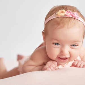 Bebê recém nascida deitada de barriga para baixo usando apenas fralda e faixa na cabeça. 